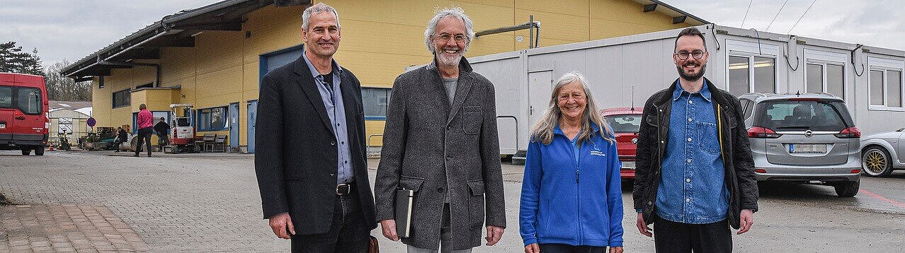 Architekt Bodo Braunmiller sowie Professor Steffen Koolmann, Sabine Mögel und Sebastian Karg von den Weckelweiler Gemeinschaften vor dem Baugelände (von links): Das beige Gebäude des Bauhofes soll energetisch saniert werden. Auf dem Platz, der noch von den Containern belegt wird, soll das neue Bildungshaus entstehen. Foto: Thorsten Hiller