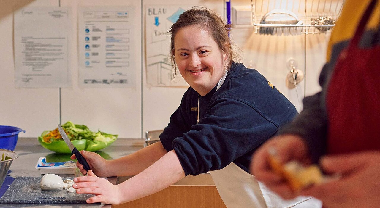 Eine junge behinderte Frau schneidet Gemüse in einer Küche